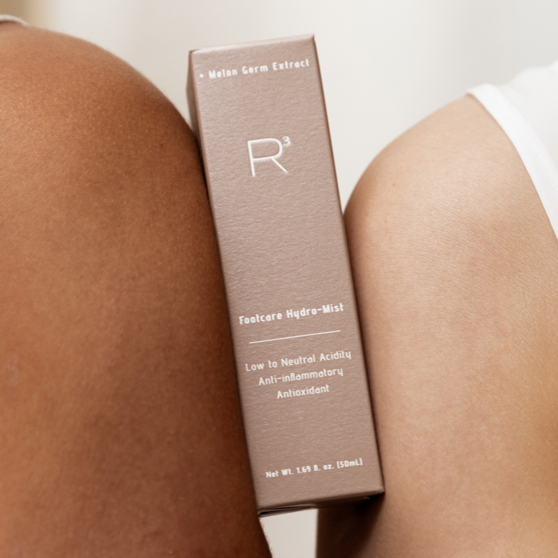 R/CUBED Foot care Hydro-Mist bottle on a light background surrounded by fresh artichokes and plums, promoting clean foot care, soft feet, and skin nourishment with plant-based ingredients